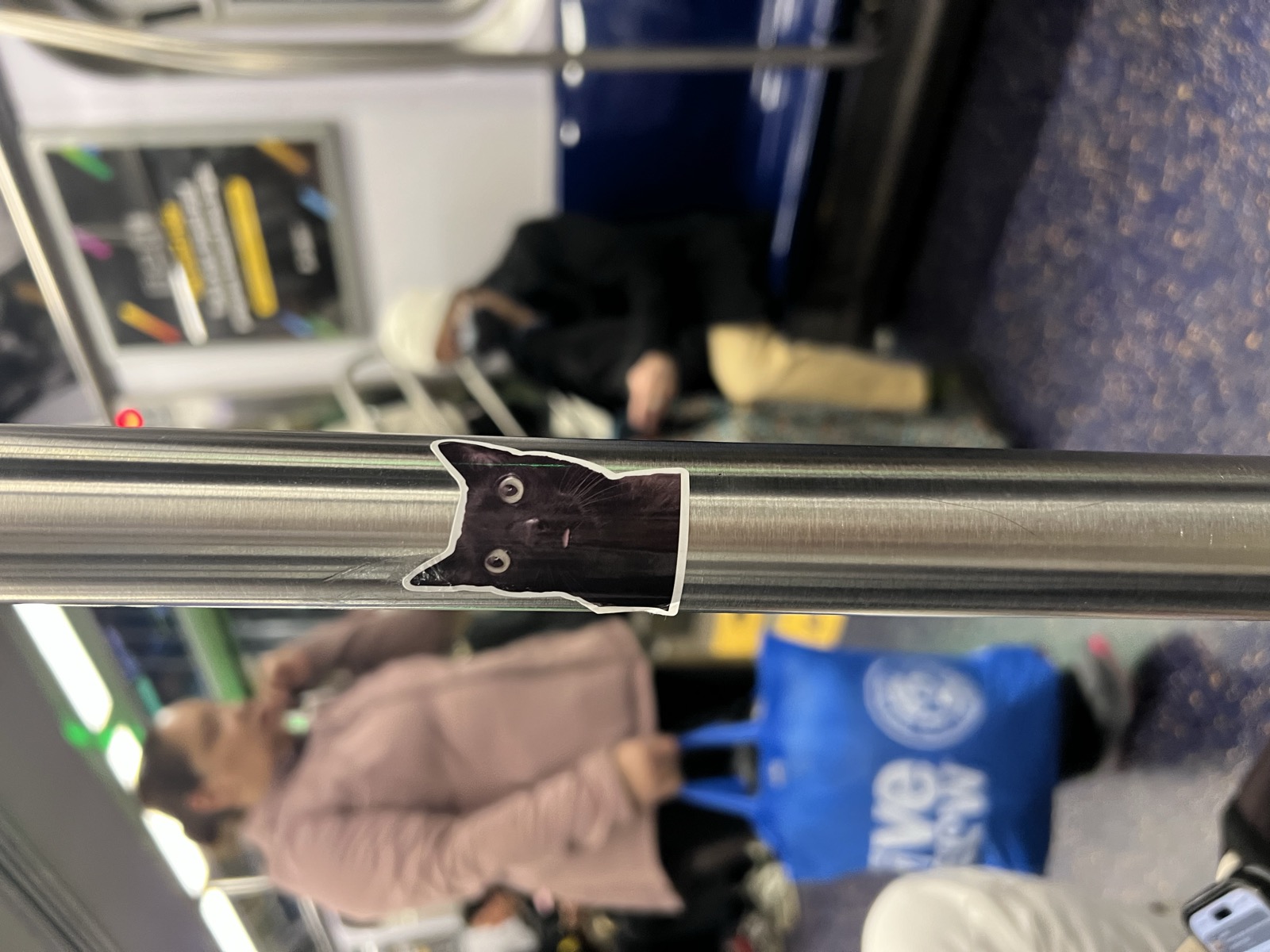 A black cat sticker on a New York subway pole, strangers around it