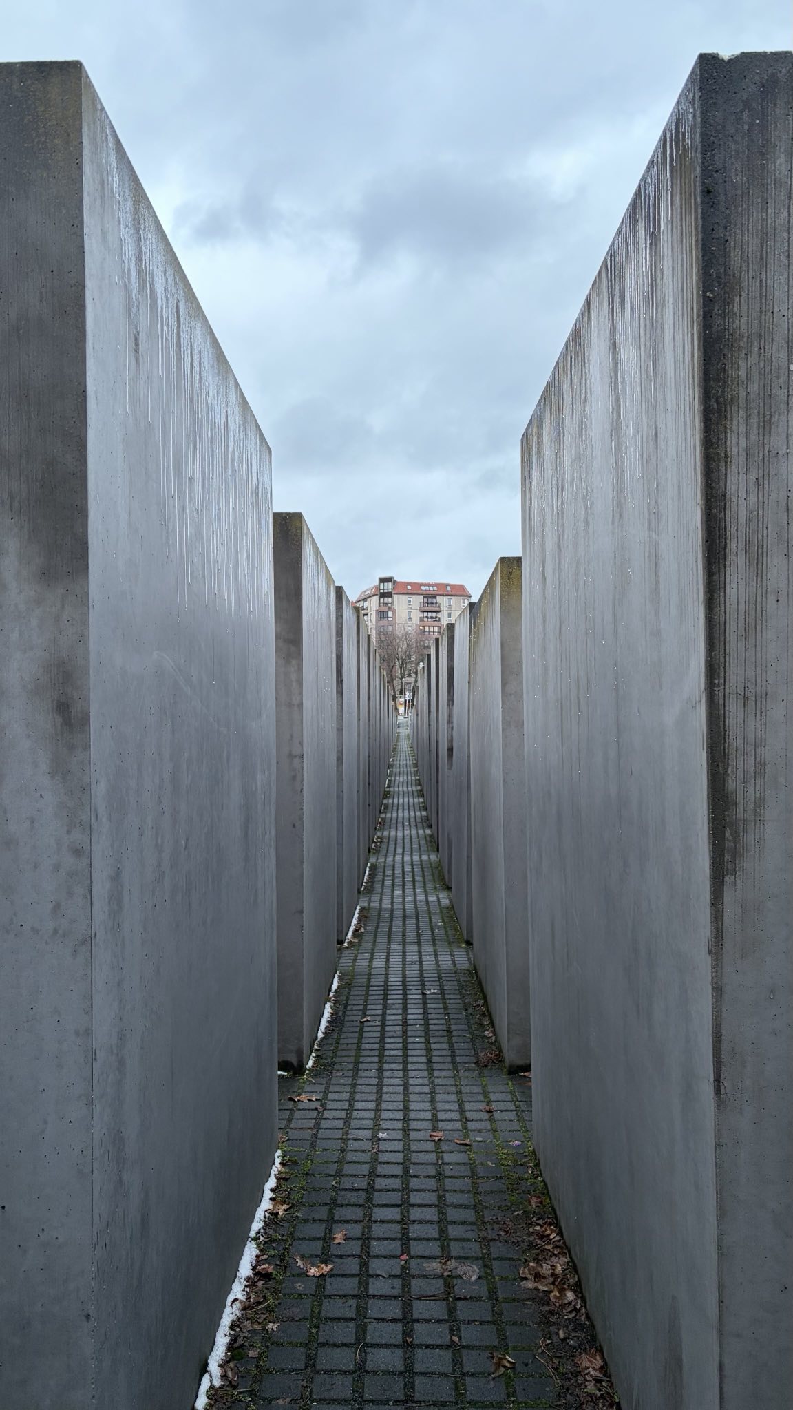 The grey concrete corridors of the Berlin memorial in winter, snow banked along one edge of the path