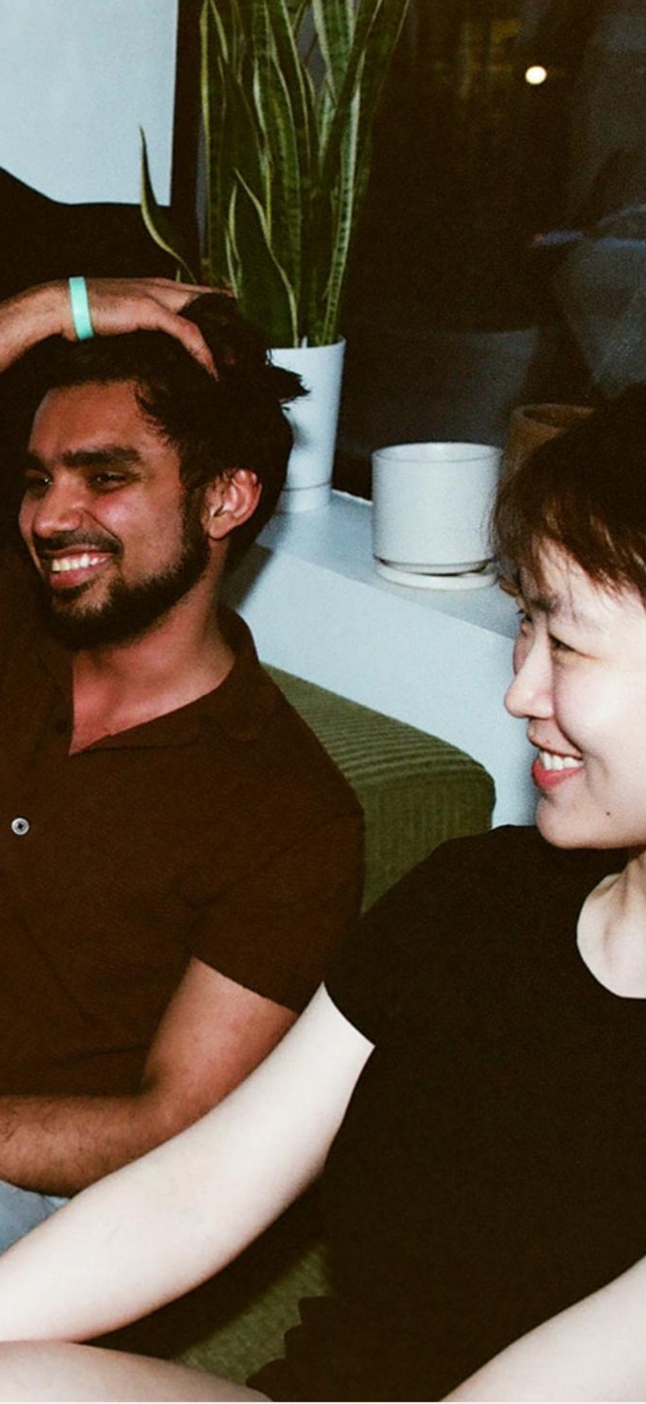 Rebecca and Shubham laughing on a couch, someone's hand on Shubham's head