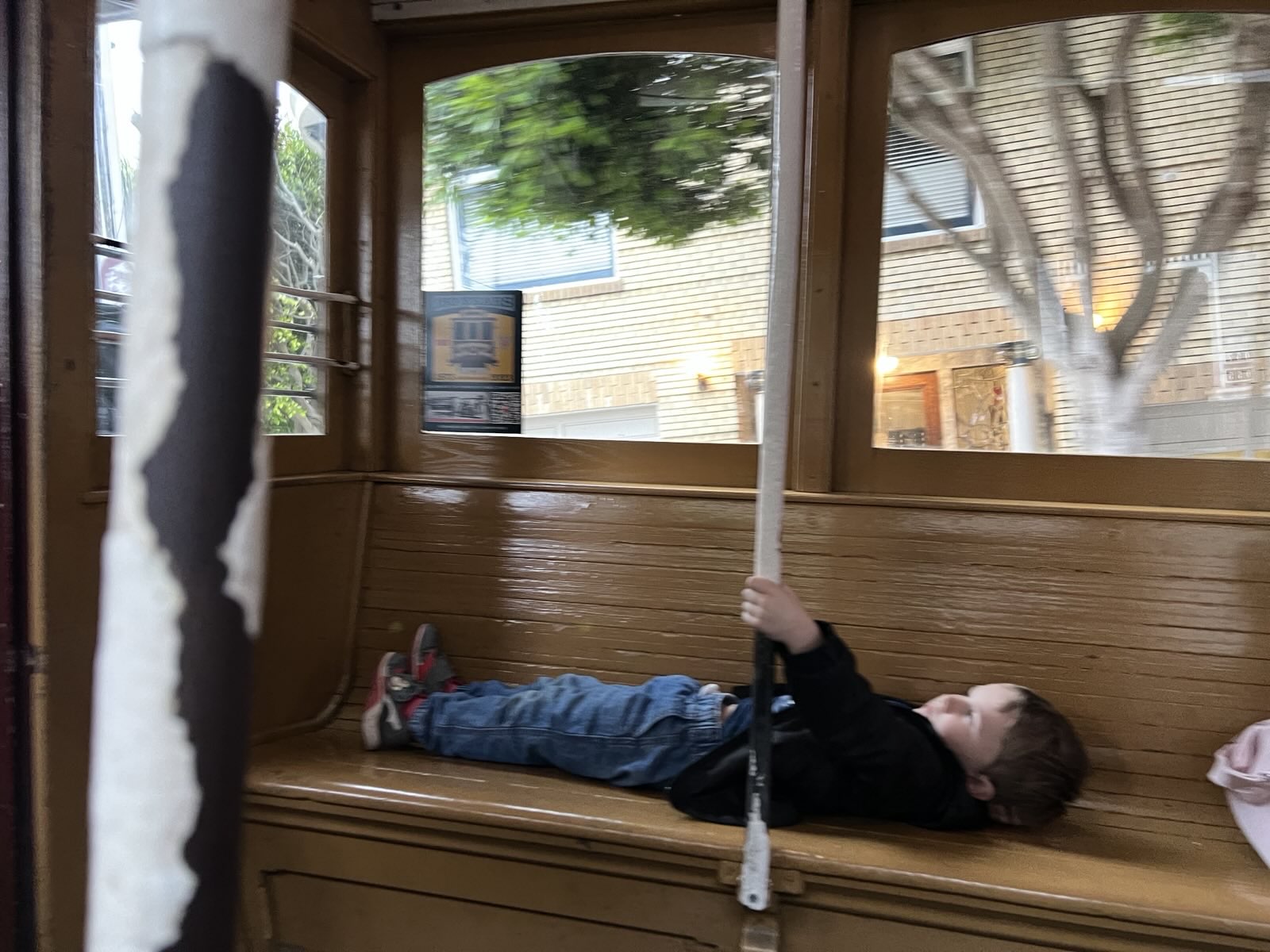 A kid flat on his back on the cable car bench, one hand on the pole like it's his job